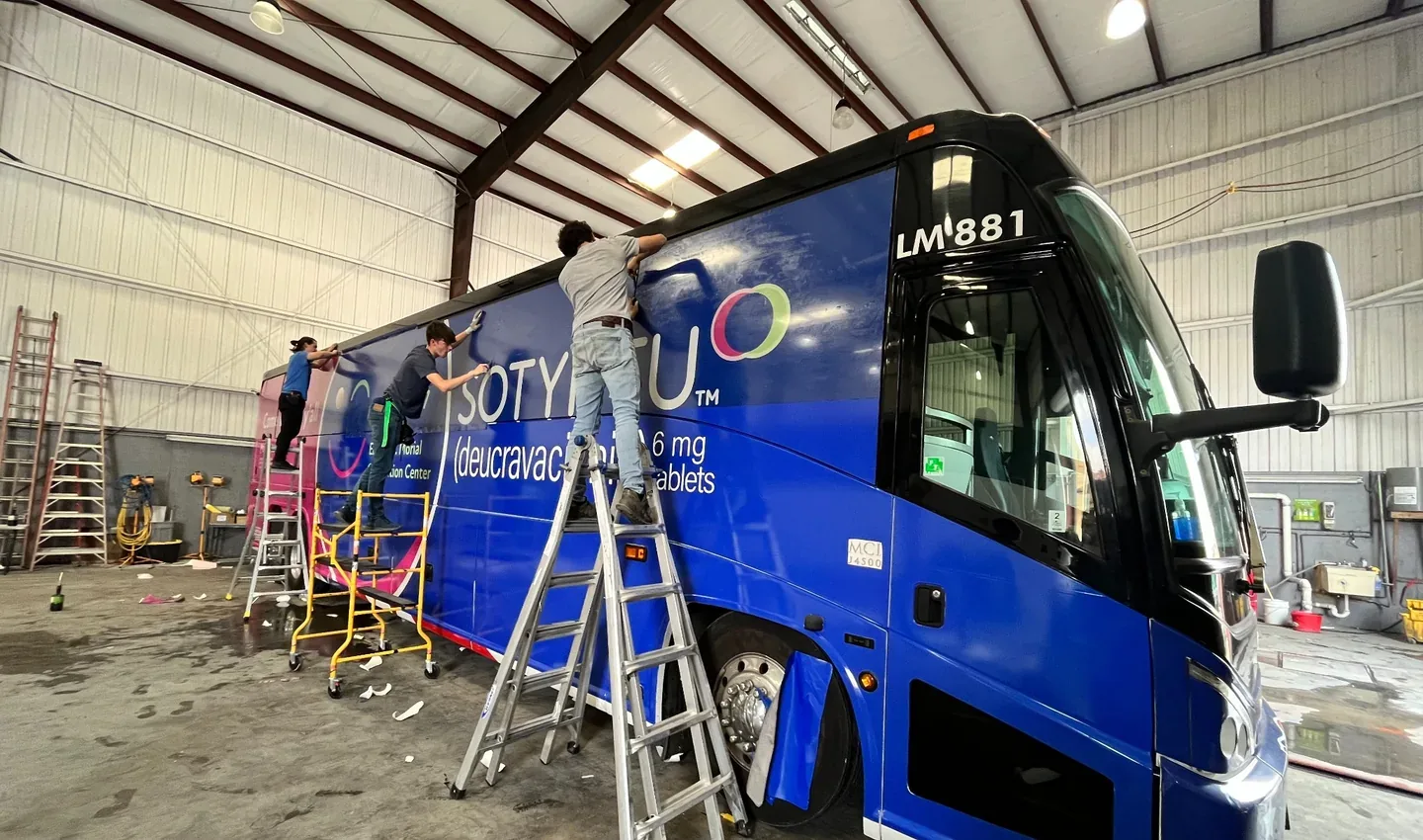 Professional installers applying printed vinyl wrap to a full-size blue bus